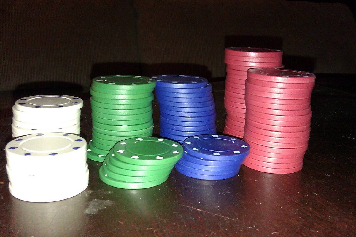 Tumpukan chip poker berwarna-warni di atas meja kayu gelap
